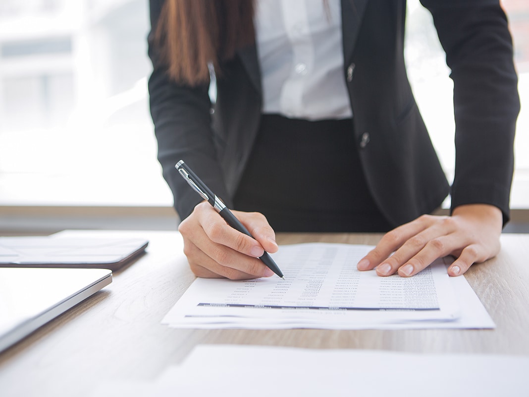 Mulher em um escritório assinando papéis de compliance enquanto segura uma caneta.